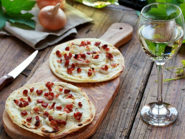 Zwei Elsässer Flammkuchen auf Holzbrett mit einem Glas Weißwein.