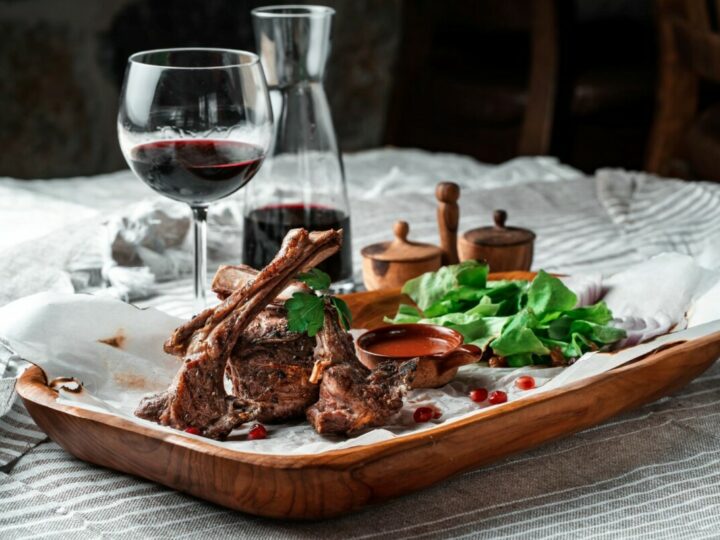 Gegrillte Lammlende auf einem Holzteller mit Salatblättern und einem Glas Rotwein.