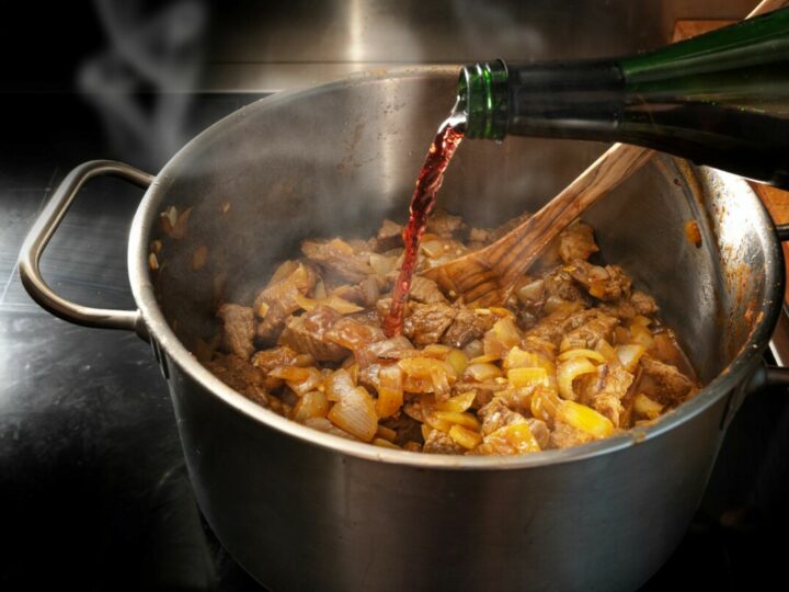Rotwein wird aus einer Flasche in einen Topf mit gebratenem Gulasch gegossen.