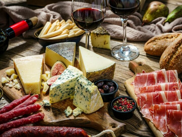 Diverse Tapas, darunter Käseplatte, Schinken und Brot, mit zwei Gläsern Rotwein.