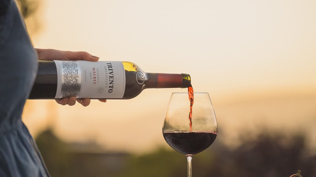 Ein Glas Rotwein wird aus einer Trivento-Flasche eingeschenkt.